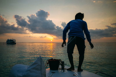 Rear view of man standing at beach during sunset