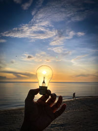 Cropped hand of woman holding balloons against sky during sunset