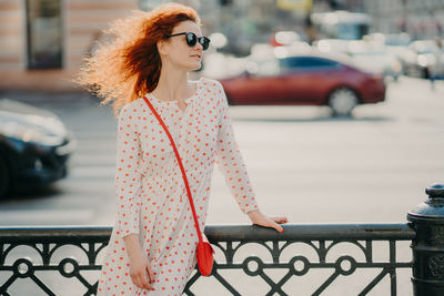 Woman looking away while standing against city in background