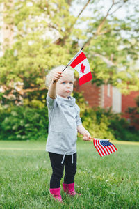 Girl holding american and canadian flag while standing on grass
