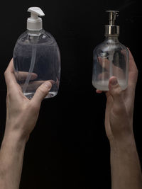 Close-up of hand holding glass bottle against black background