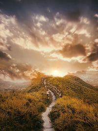 Dirt road passing through landscape against cloudy sky