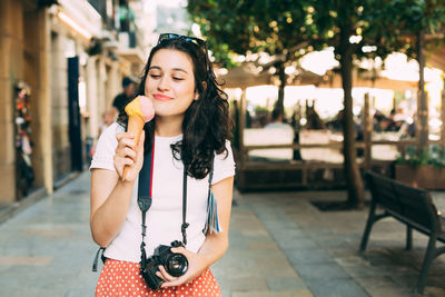 Portrait of young woman holding ice cream standing in city