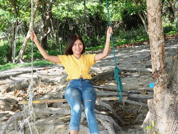 Full length portrait of smiling young woman standing in park