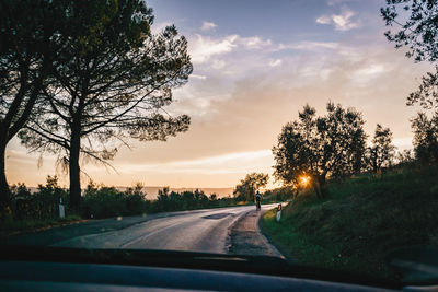 Road by trees against sky seen through car windshield