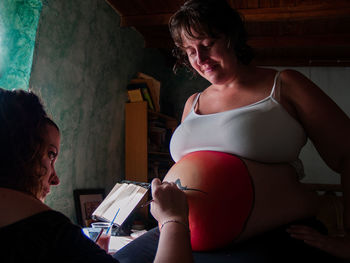 Woman painting on pregnant friend belly
