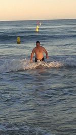 Shirtless man in sea against sky during sunset