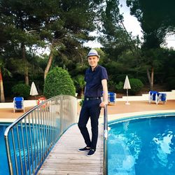 Full length portrait of smiling young man standing at swimming pool