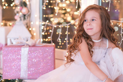 Little beautiful girl sitting on the windowsill, looking and smiling on lights background. new year.