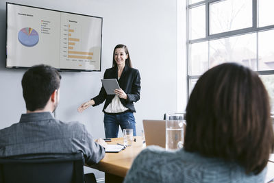 Confident businesswoman giving presentation to colleagues in meeting at board room