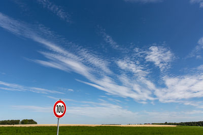 Road sign on field against blue sky