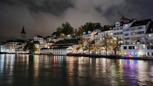 Buildings by river against cloudy sky