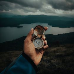 Midsection of person holding compass against mountain