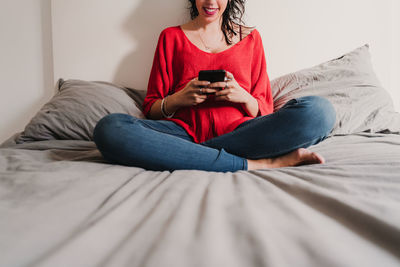 Midsection of man using mobile phone while sitting on bed at home