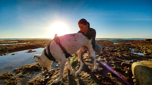 Woman with dog at beach against sky during sunset