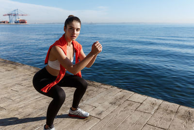Full length of woman exercising by railing against sea