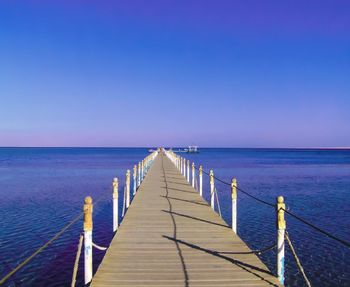 Pier over sea against clear blue sky