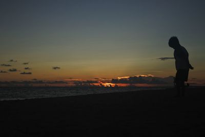 Silhouette man standing on beach against sky during sunset