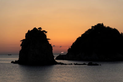 Silhouette rock formation in sea against sky during sunset