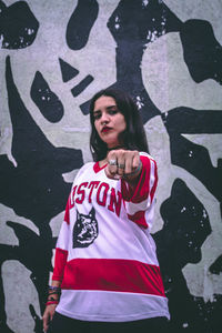 Portrait of woman gesturing while standing against graffiti wall