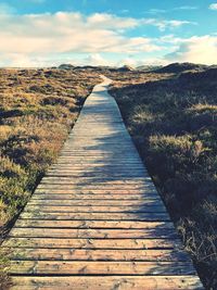 Boardwalk leading towards landscape against sky