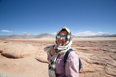 Portrait of woman standing on sand at desert against clear sky
