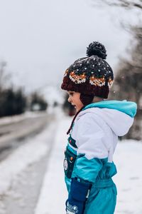 Side view of girl standing on snow covered field against sky