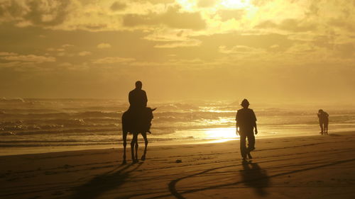 Silhouette people on beach against sky during sunset