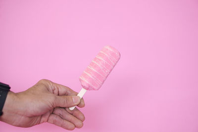 Midsection of person holding ice cream against pink background