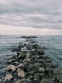 Groyne in sea against cloudy sky