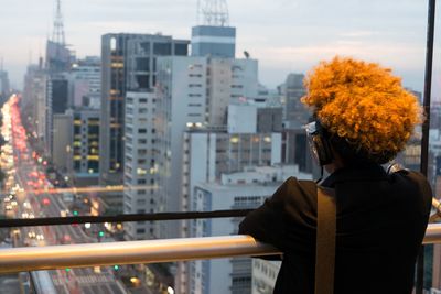 Rear view of man standing by railing against buildings in city