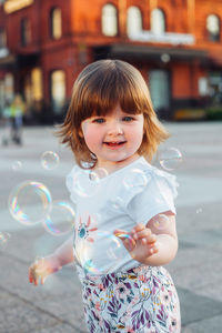 Little girl playing on the street with blowing soap bubbles