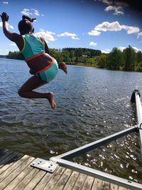 Rear view of girl jumping in lake against sky