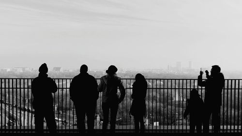 Rear view of silhouette people standing by railing against cityscape