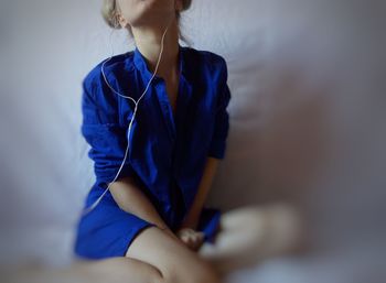 Midsection of young woman listening music while sitting on bed