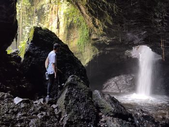 Man standing on rock by waterfall