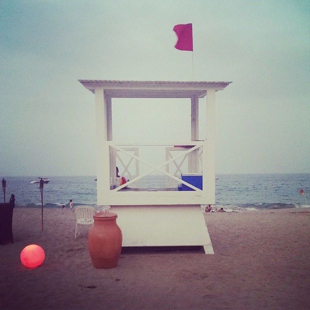 sea, horizon over water, beach, water, flag, built structure, architecture, sky, shore, building exterior, sand, day, tranquility, nature, clear sky, tranquil scene, red, outdoors, no people, scenics