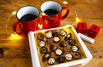 Two cups of coffee in red cups on a background of chocolate canfet. postcard with date and month. 