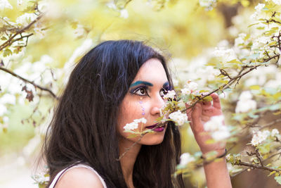 Close-up of young woman with eye make-up smelling flowers