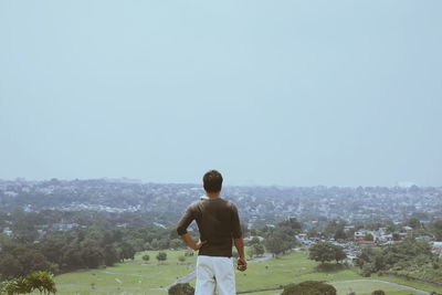 Rear view of man standing on golf course against clear sky