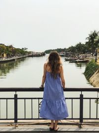 Rear view of woman standing on bridge over lake against sky