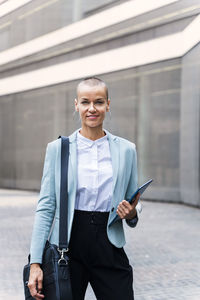 Smiling businesswoman with tablet pc standing on footpath