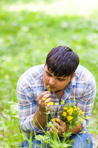 Rear view of man holding flowering plant on field