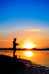 Silhouette man fishing in sea against sky during sunset