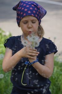 Girl blowing dandelions while standing on field