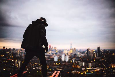 Rear view of man standing against cloudy sky in city