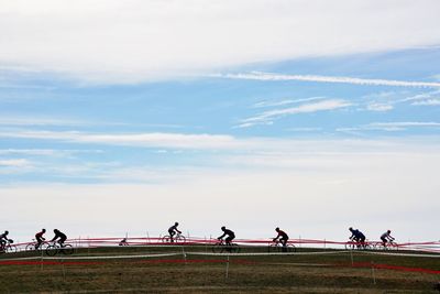 People riding bicycles on field against sky