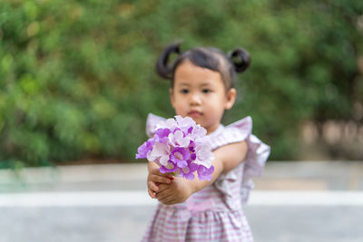 Portrait of girl holding bunch of flowers while standing outdoors