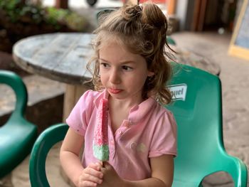 Innocent girl holding ice cream while sitting on chair