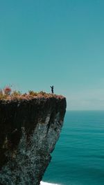 Man standing at cliff by sea against clear blue sky